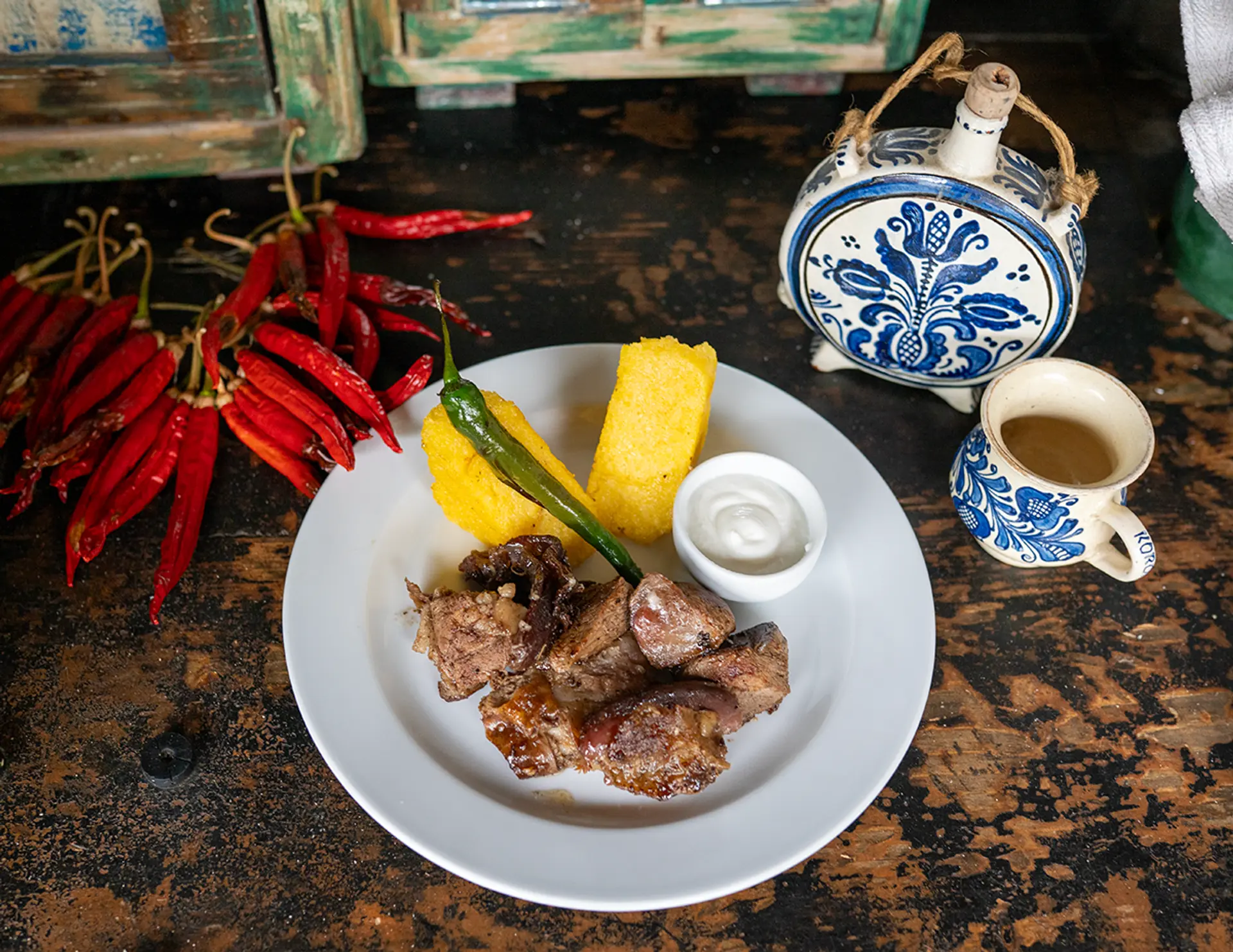 Rustikaler Teller mit Fleisch, Mămăligă und Chili auf dunklem Tisch
