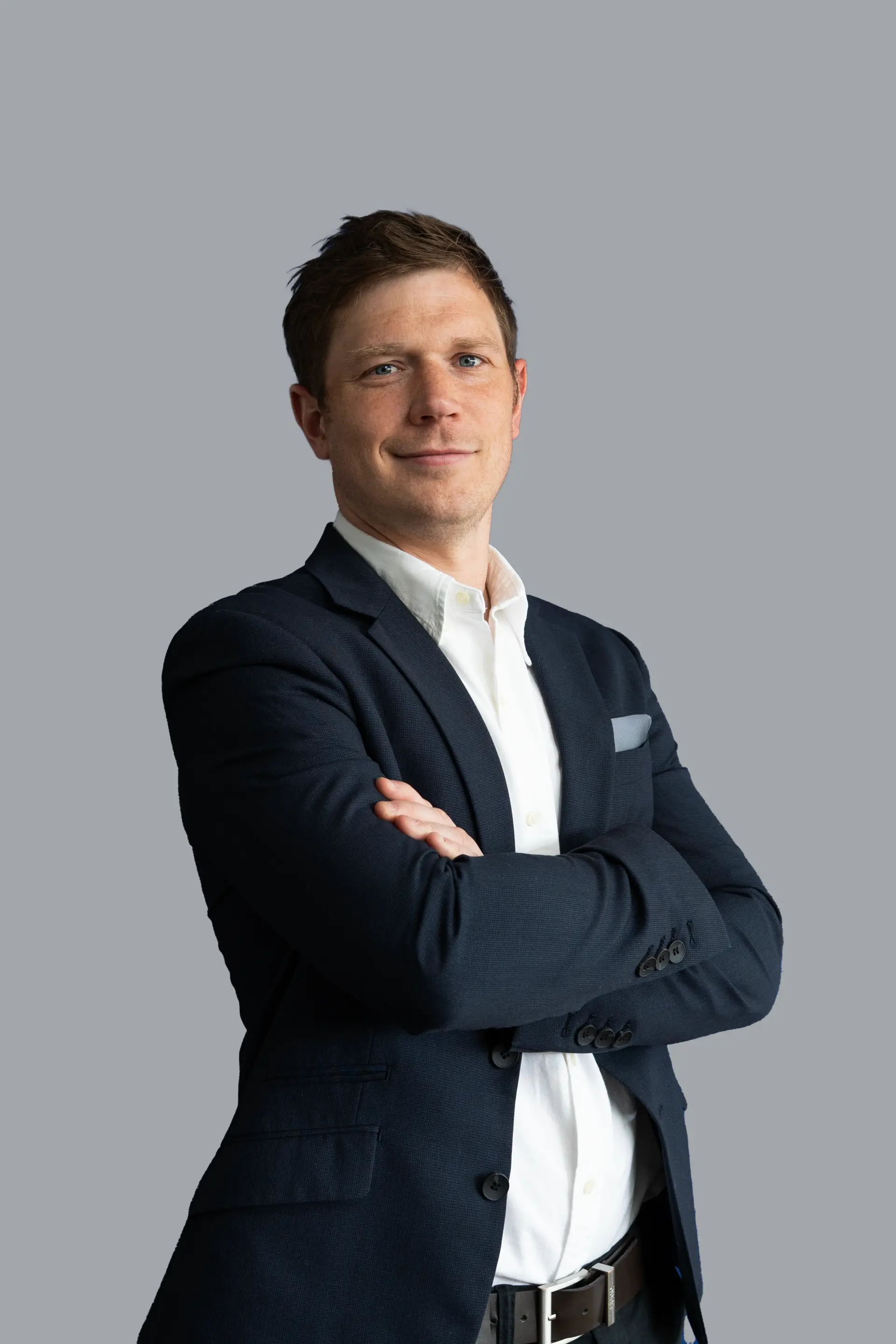 Mann im dunklen Sakko mit verschränkten Armen vor grauem Hintergrund, Business-Porträt