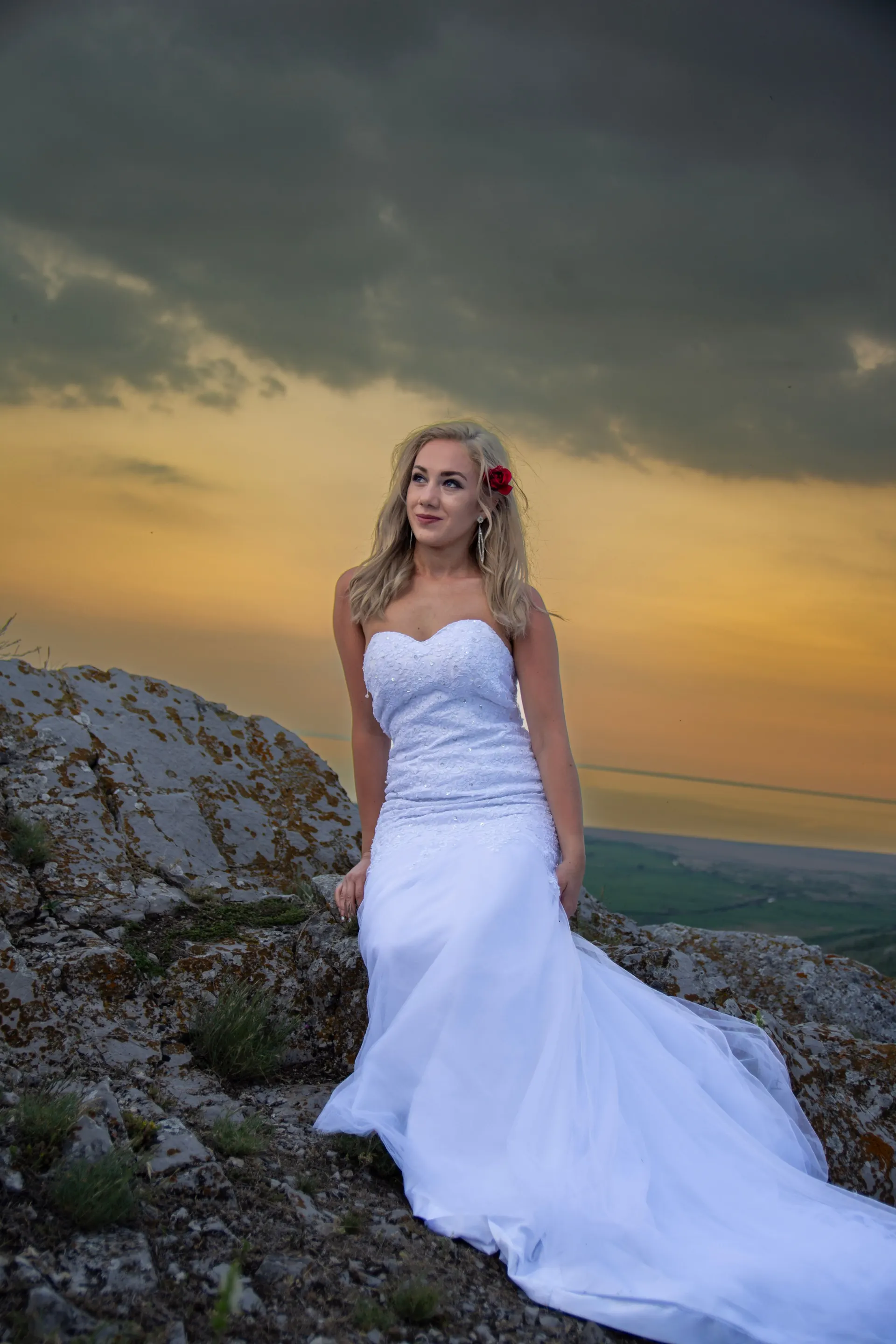Braut im trägerlosen Brautkleid auf einem Felsen vor orangem Abendhimmel