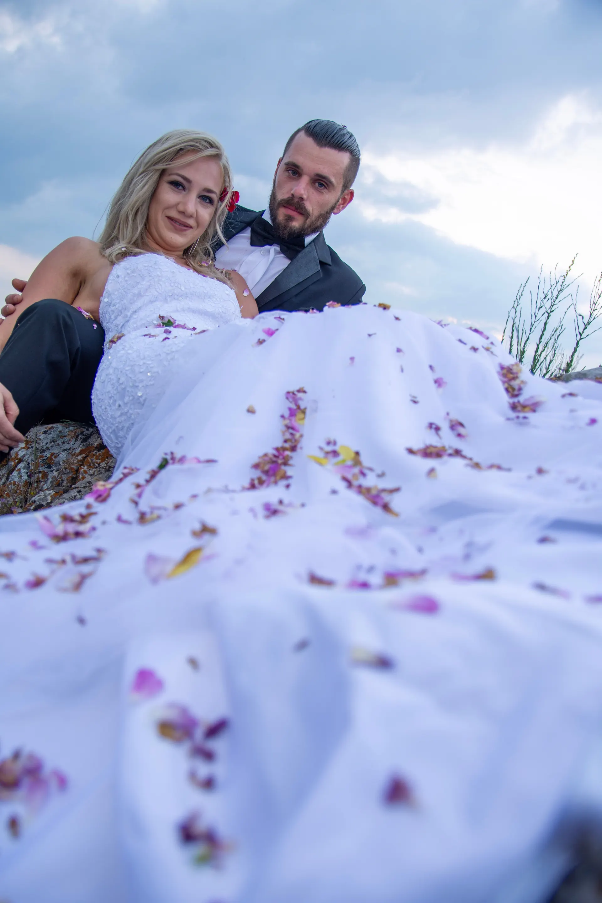 Brautpaar liegt auf den Felsen, Blütenblätter auf dem Brautkleid