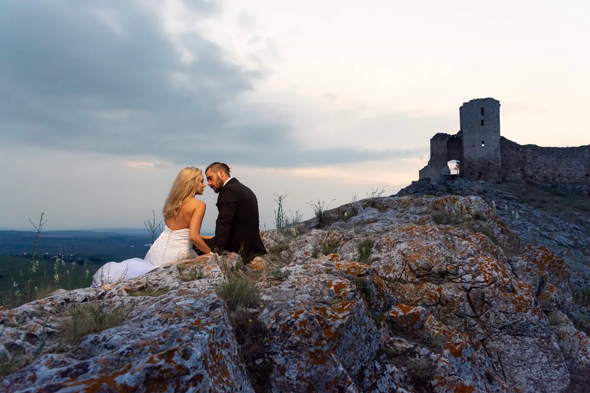 Paar sitzt eng umschlungen auf einem Felsen, im Hintergrund die Festung Enisala