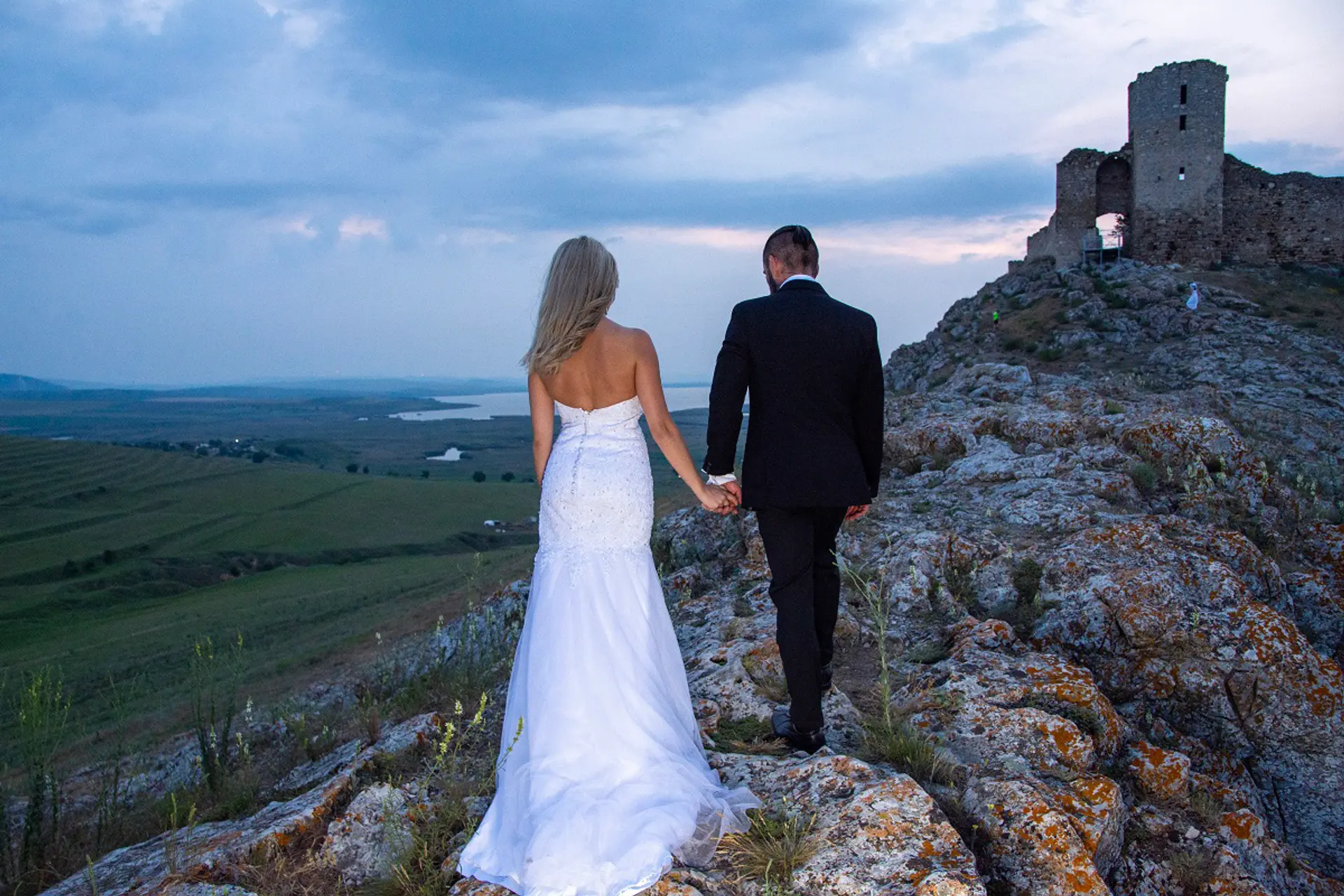 Paar in Brautkleid und Anzug geht Hand in Hand über die Felsen an der Festung Enisala