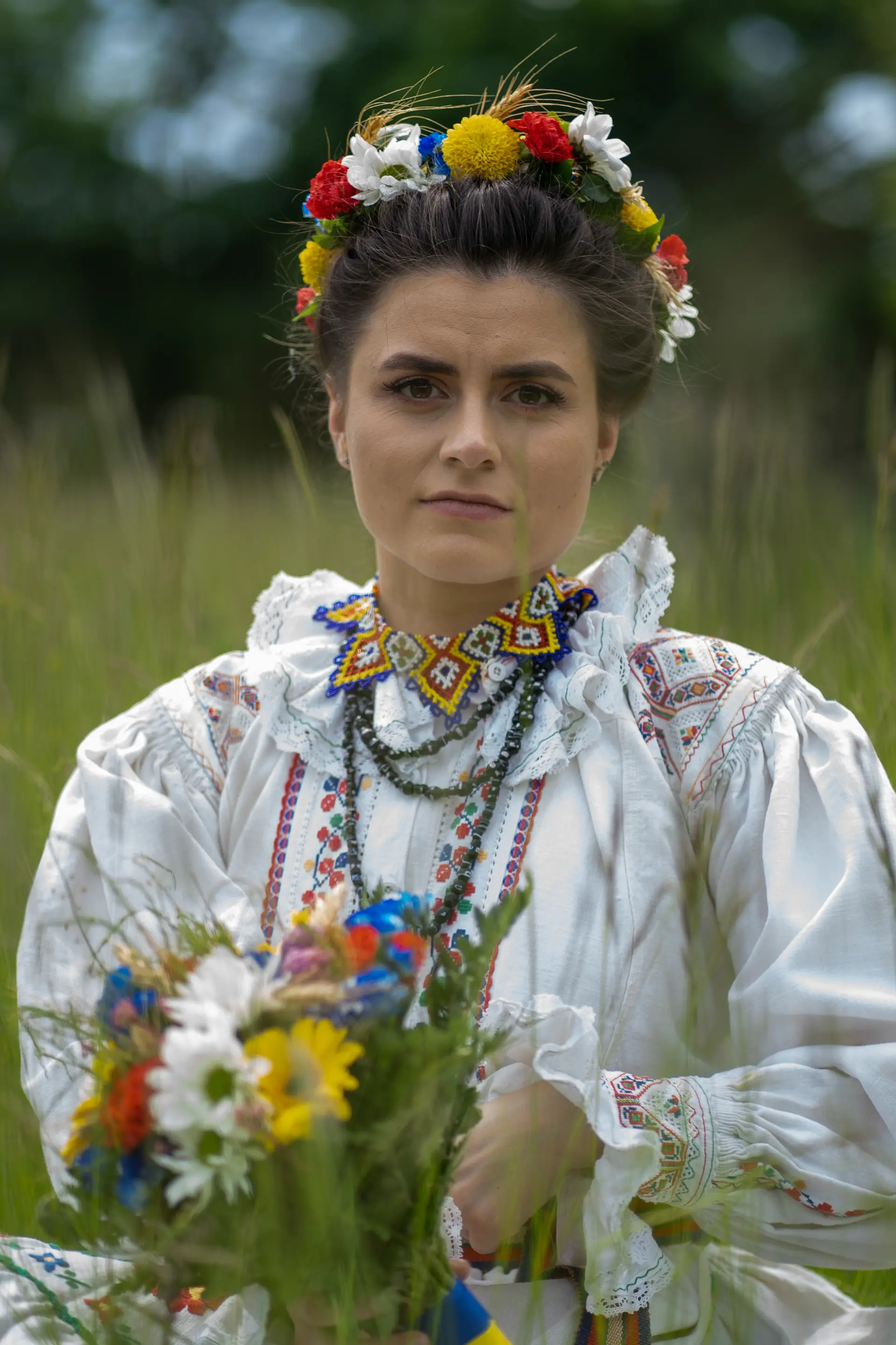 Frau in rumänischer Tracht mit Blumenkranz und Wiesenblumen auf einer Wiese