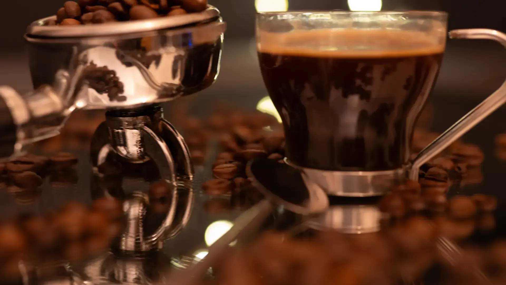 Espresso in einer Glastasse neben einem Siebträger voller Kaffeebohnen